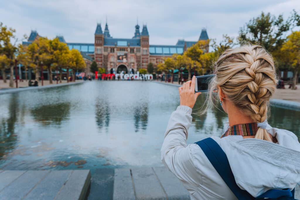 Woman tourist taking photo of the Rijksmuseum in Amsterdam on the mobile phone. ETIAS Update.