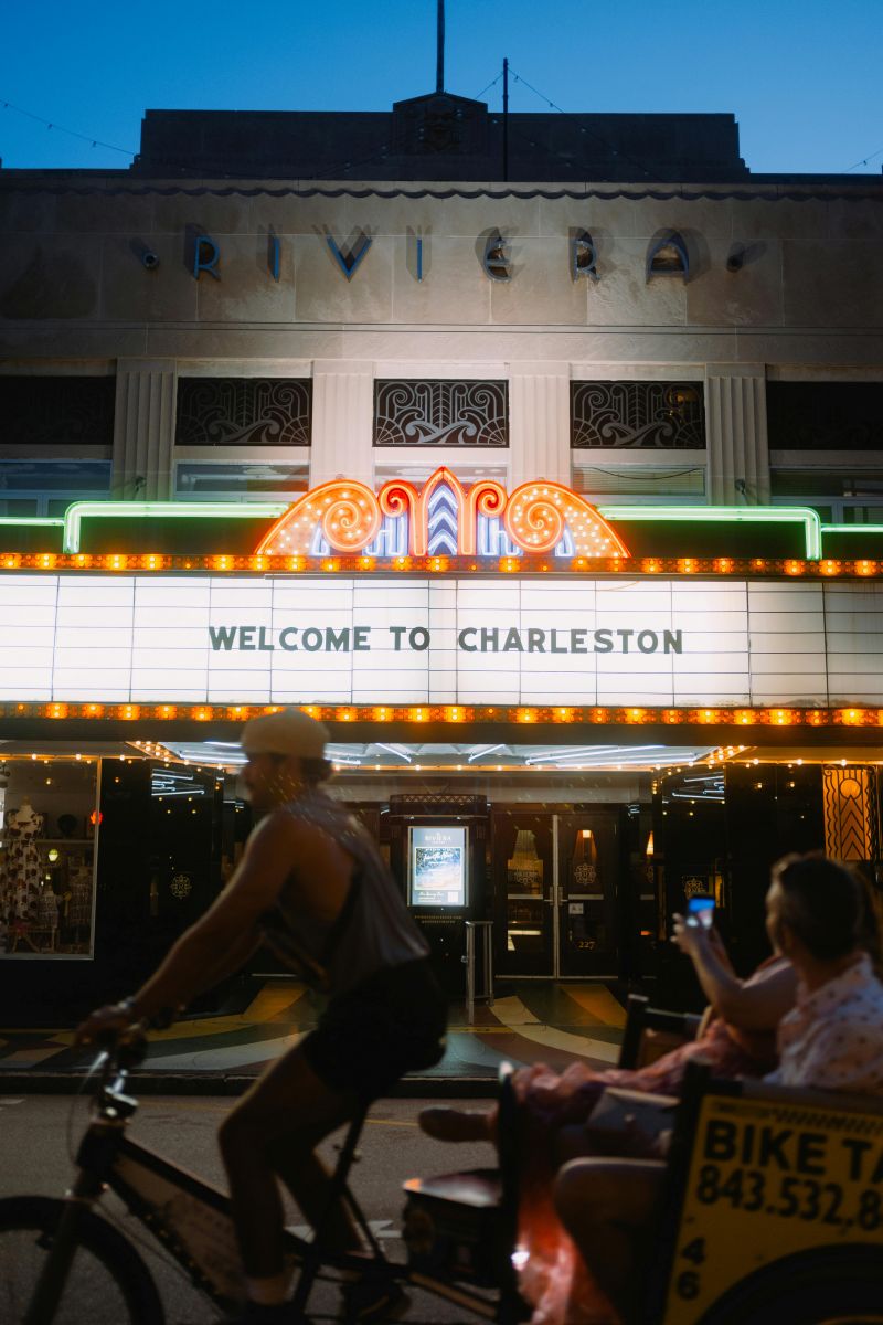Welcome to Charleston, Vibrant blue hour scene at the iconic Charleston Riviera Theater with neon lights and pedestrians.
Photo Credit: Tolga Ahmetler