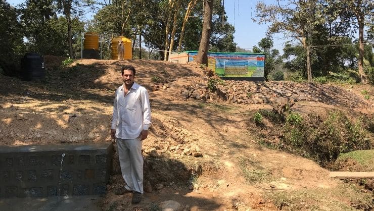 Miles standing next to the water distribution location in Nersa, India