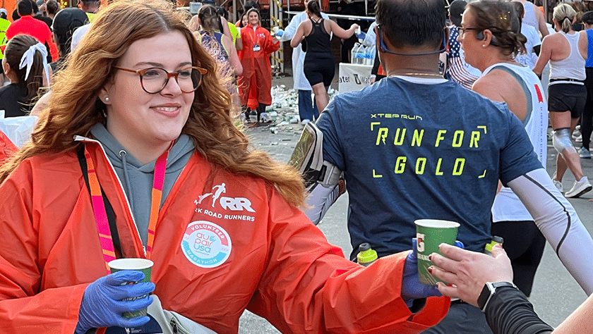 Young woman in orange poncho hands Gatorade to a marathon runner.