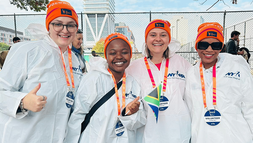 Four young women smile while wearing marathon volunteer ponchos and ski caps.