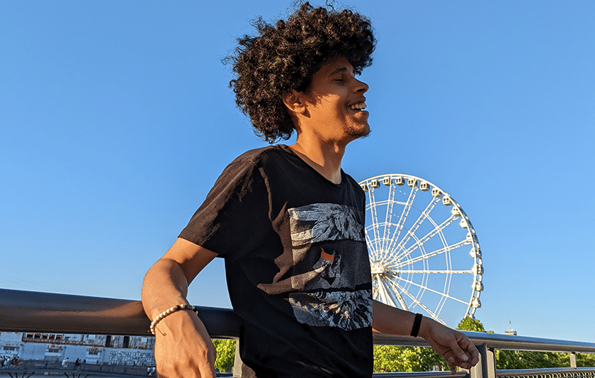 Smiling young man visits Montreal's old port with ferris wheel in background.