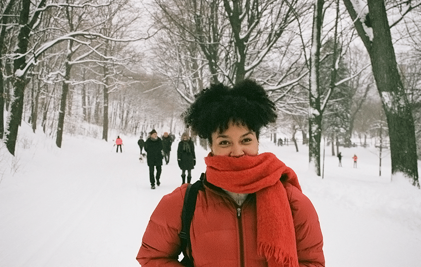Young woman in red scarf walks through snow-covered park in Montreal.