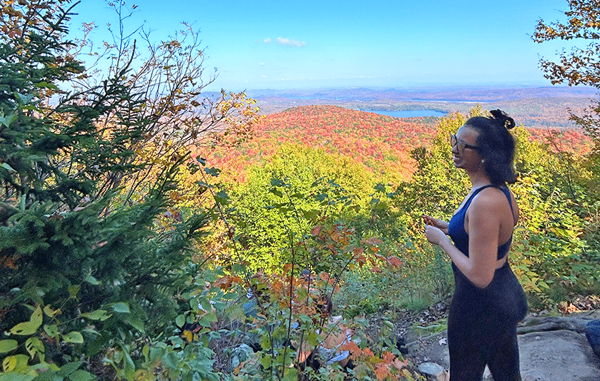 Smiling young woman in sunglasses overlooks autumn foliage in Parc national du Mont-Orford, Quebec.