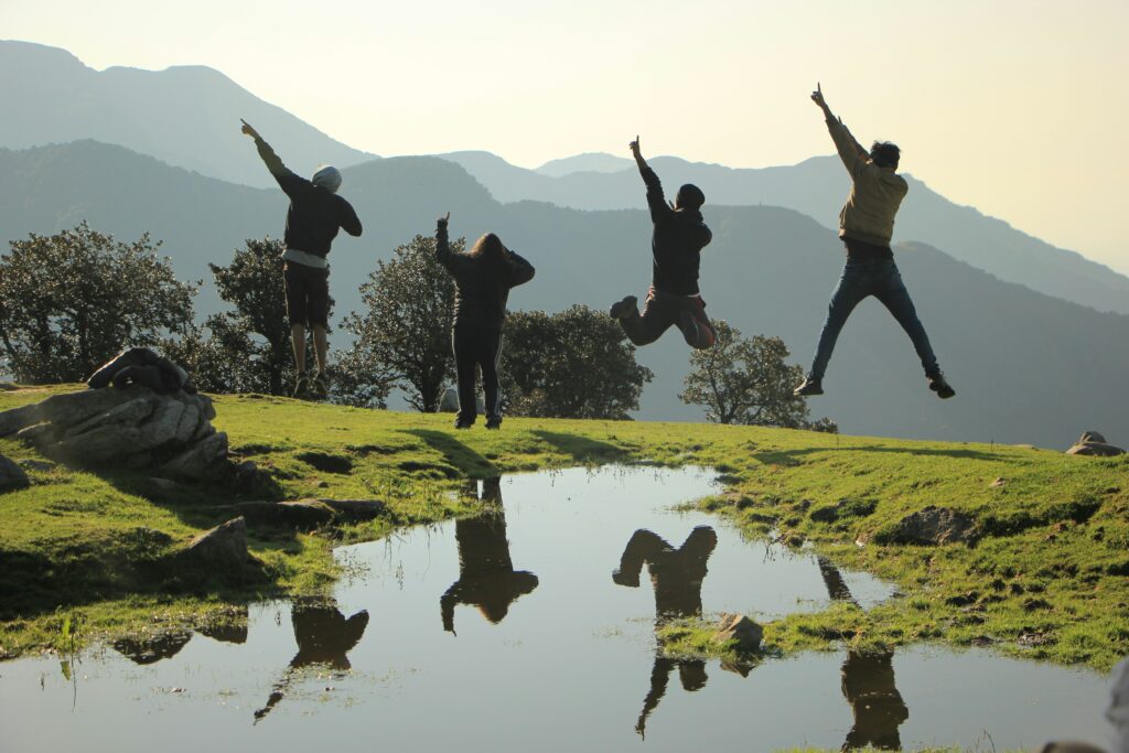 Four young people jumping above a lake with a scenic mountain backdrop.