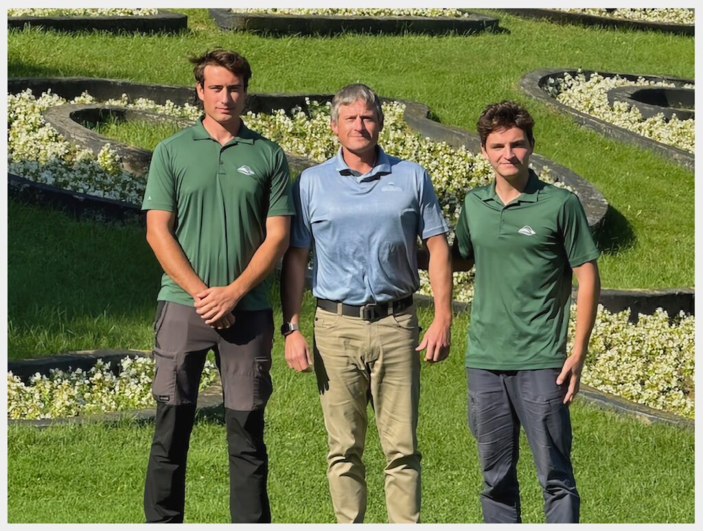 Three coworkers posing on a golf course, wearing employee uniforms.